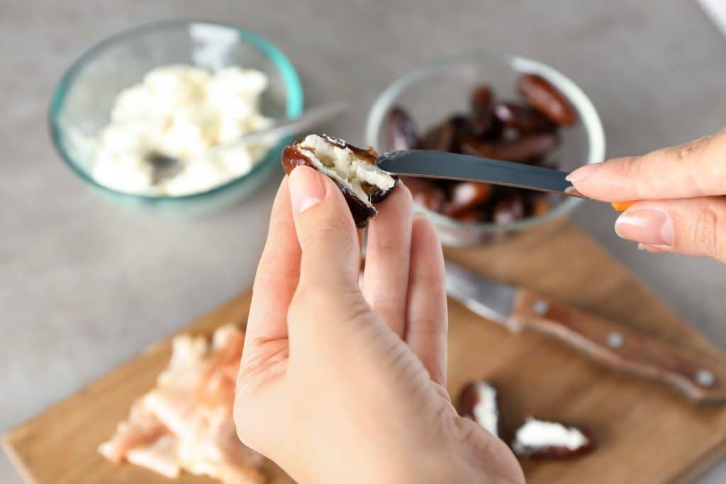 hands filling a date with creamy nut butter for stuffed dates snack