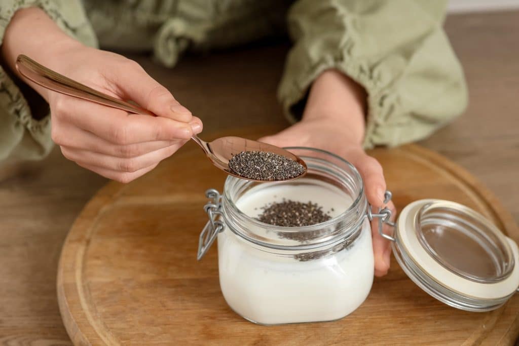 Hand spooning chia seeds into milk jar for chia pudding snack recipe