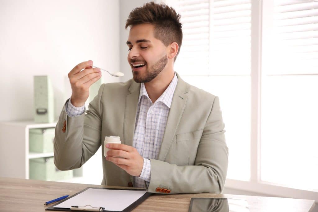 Man eating yogurt at his desk as part of healthy office snacks