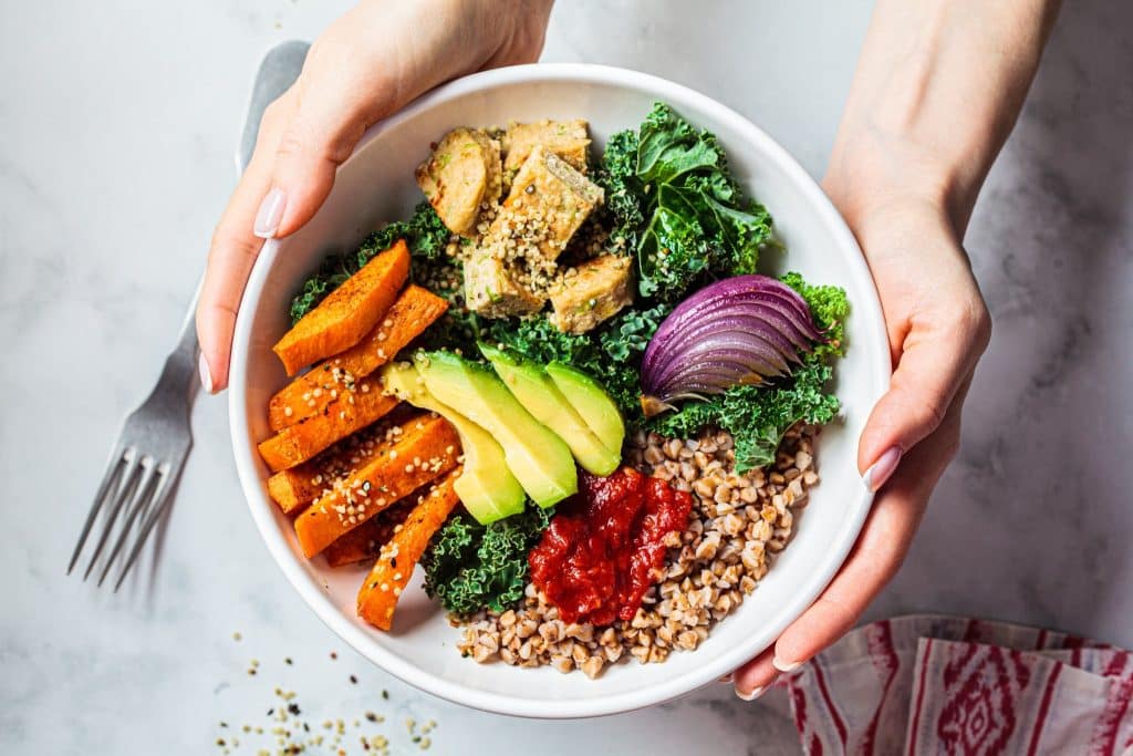 Hands holding a grain and veggie bowl sprinkled with hemp seeds