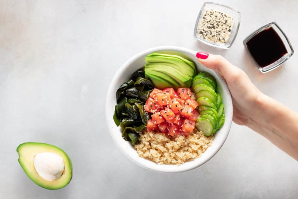 Hand holding a salmon quinoa bowl with avocado and cucumber for tyrosine foods Hand holding a salmon quinoa bowl with avocado and cucumber for tyrosine foods dopamine lunch idea.