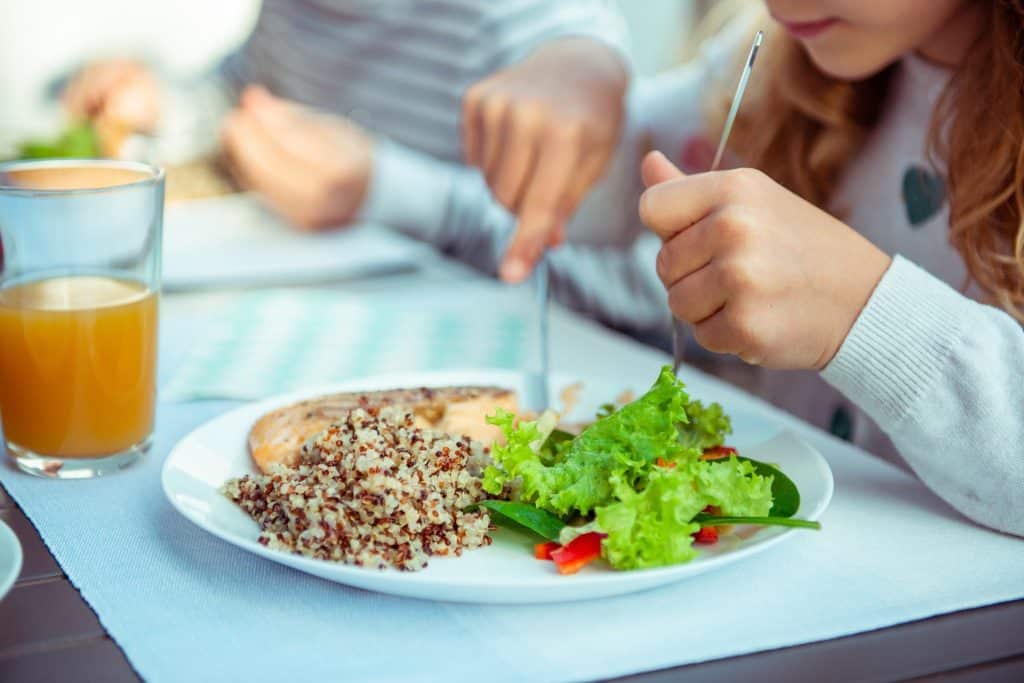 Child enjoying quinoa salad with fresh vegetables, illustrating the long-term health benefits of ancient grains for families.