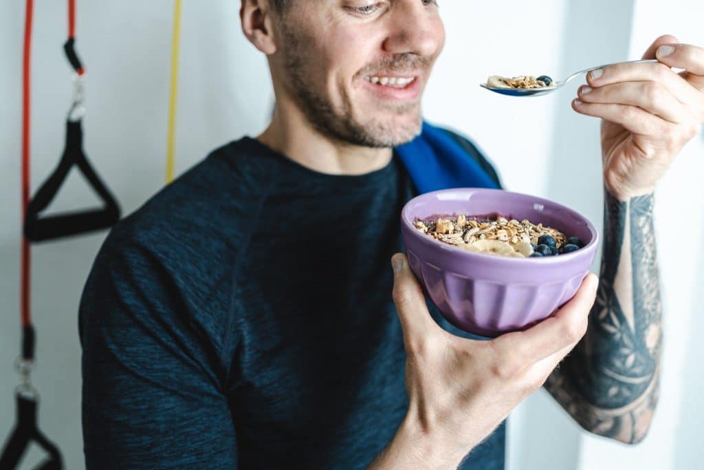 Man holding a nutritious smoothie bowl with granola and berries, promoting gut health as part of a diet for anxiety and depression.