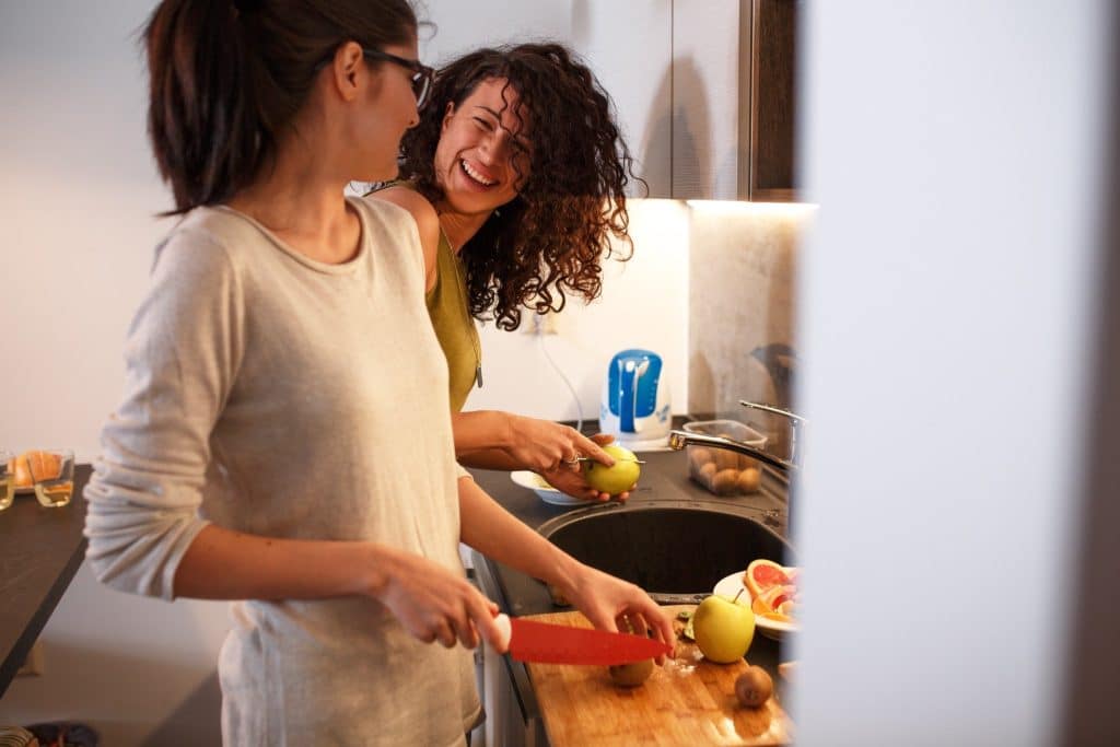 Two friends laughing together while preparing healthy fruits in the kitchen, highlighting the social benefits of a diet for anxiety and depression.