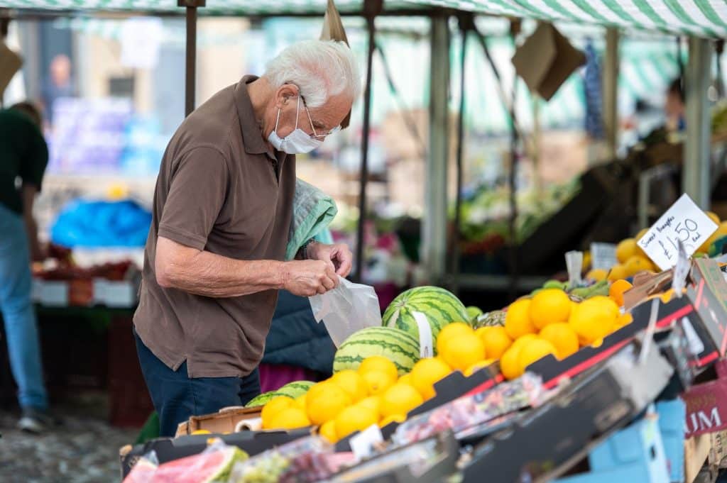 Older man wearing a mask buying fresh produce at a farmers’ market, showing how the food choices pandemic boosted local food movements.