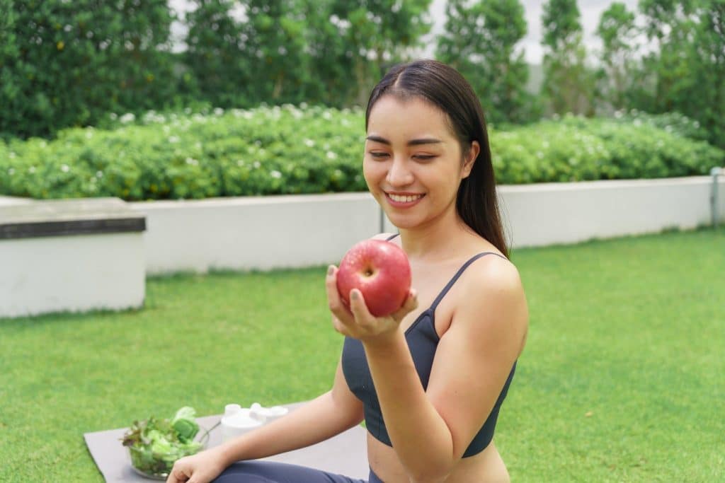 Woman in fitness clothes smiling while holding a red apple outdoors, highlighting apples as one of the best fruits for energy.