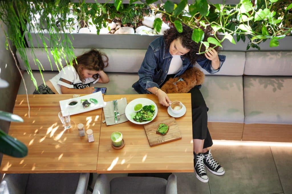Mother and child dining together with fresh green meals in a nature-inspired café, reflecting family choices in the future of clean eating.