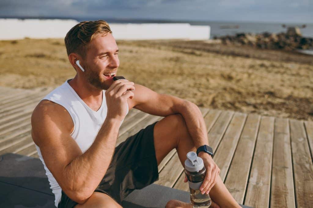Man enjoying homemade energy bars after a workout outdoors with water bottle.