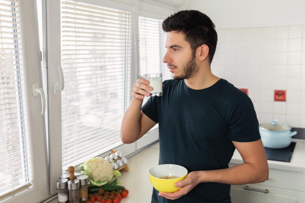 Man drinking kefir with breakfast near window.