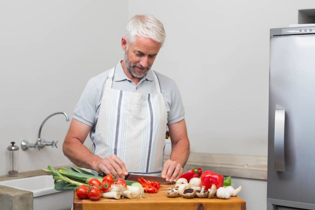 Man chopping leeks, garlic, and vegetables on a kitchen board