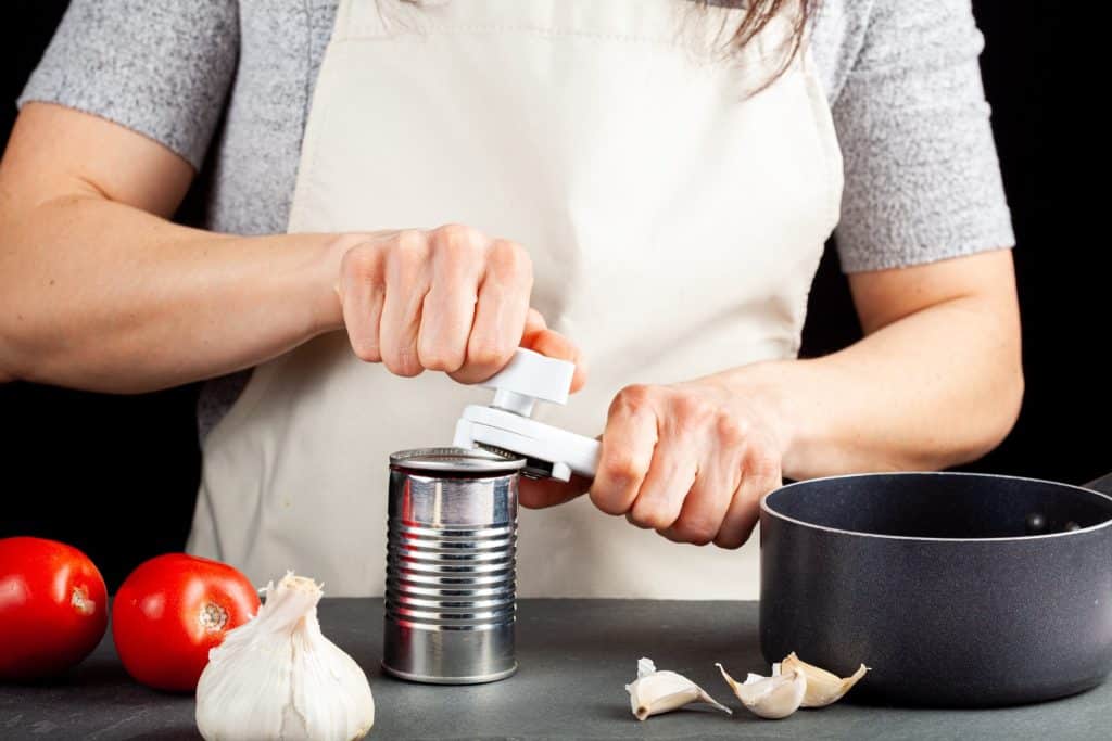 tinned fish trend pantry planning: hands opening canned peas in a bright kitchen; easy shelf-stable meals.