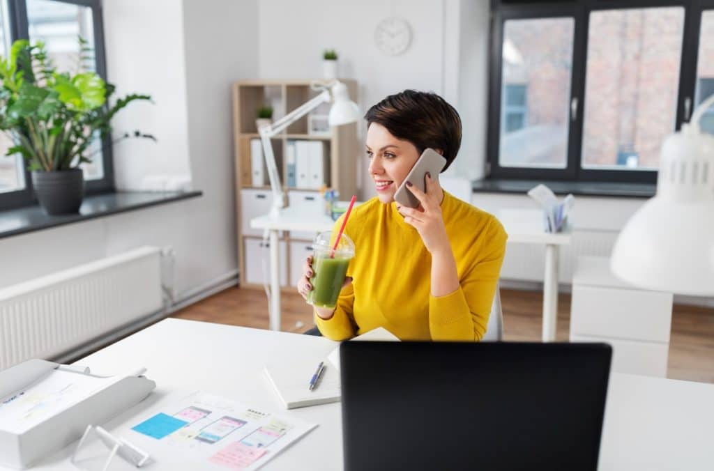 woman on a phone call drinking a green smoothie at her desk