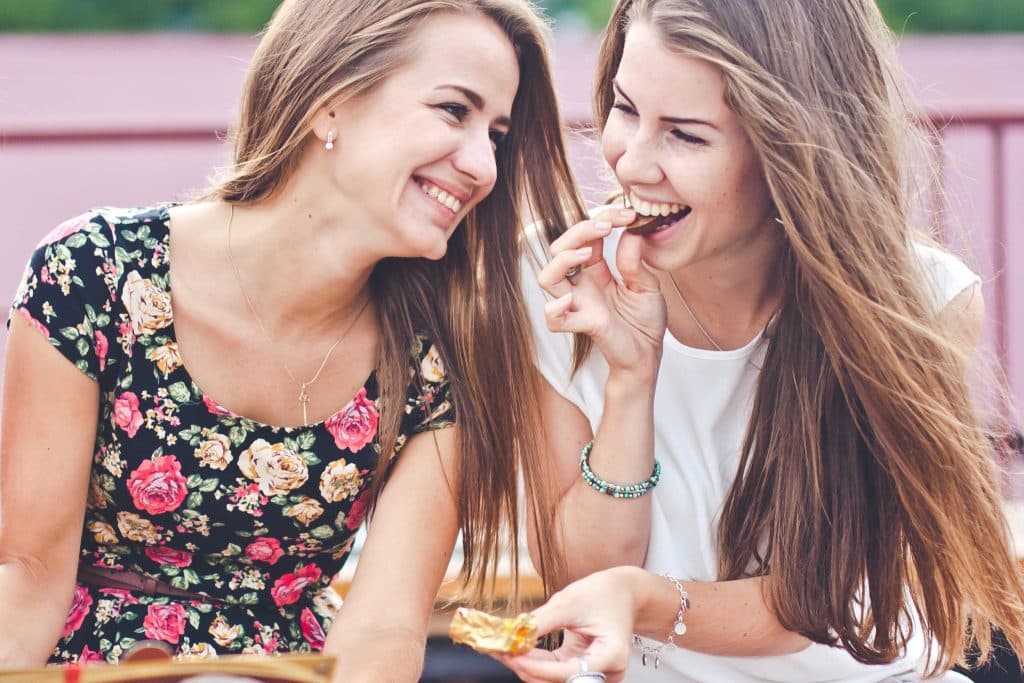 Two friends laughing and sharing dark chocolate for brain and mood outdoors.
