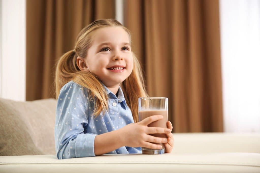 Happy child holding a glass of chocolate drink linked to the idea of dark chocolate for brain and mood.