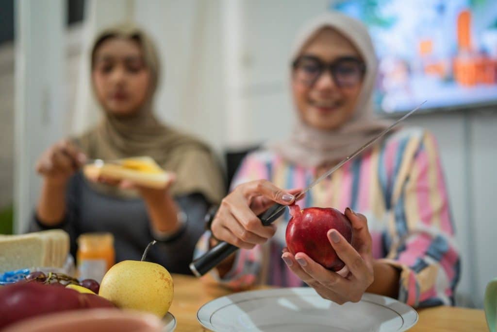 Two women preparing fruit and discussing high-protein low-carb snacks at home.