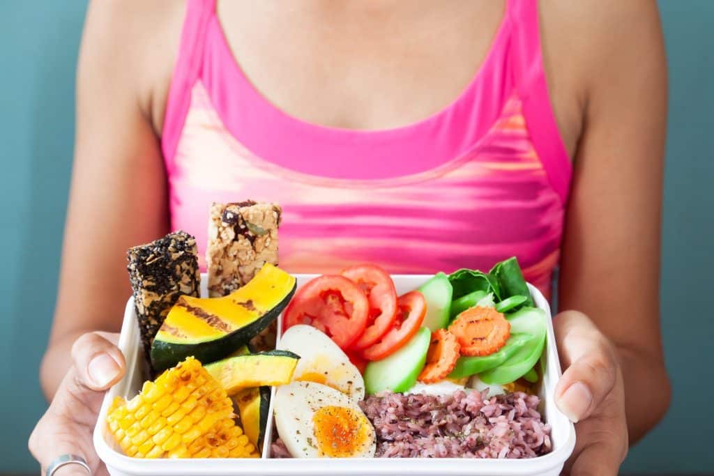 Woman holding a container of high-protein low-carb snacks with eggs, vegetables, and grains.