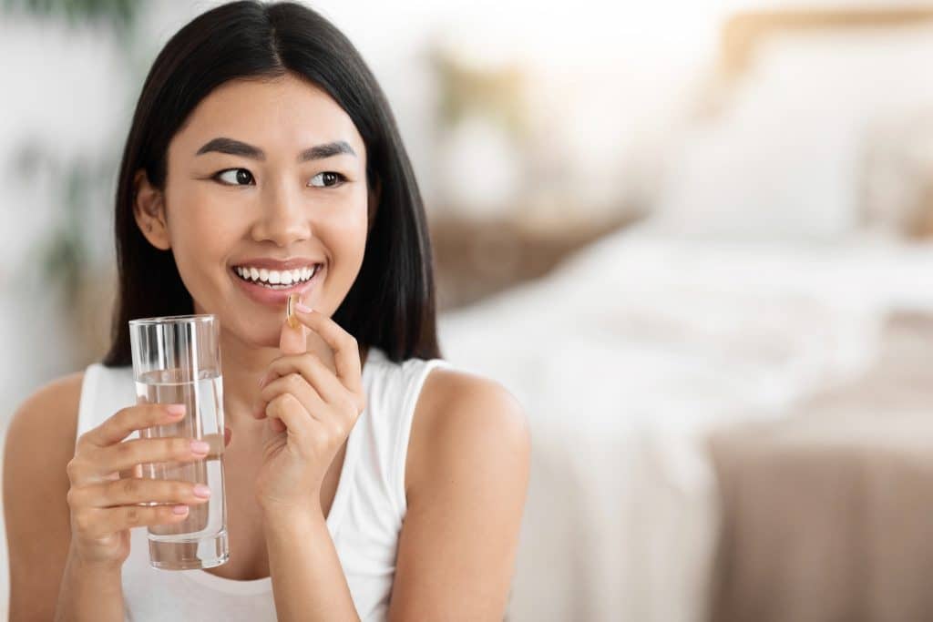 Woman taking a fish oil capsule with a glass of water