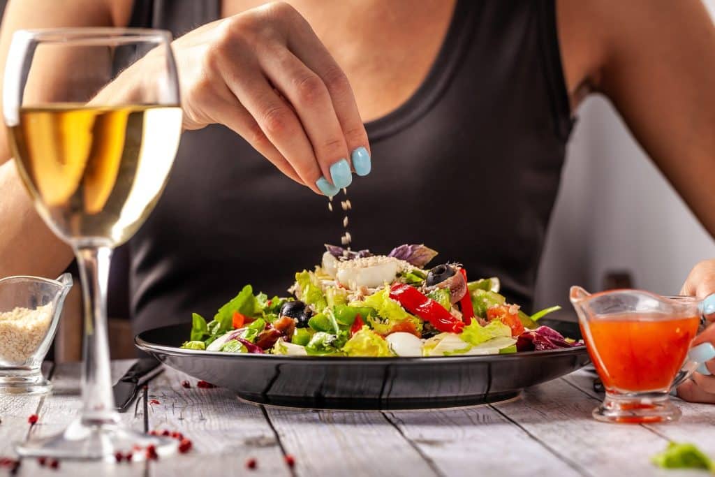 Sprinkling seeds over a colorful salad with olives and anchovies