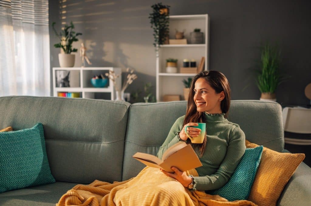 Woman enjoying tea rich in polyphenols in health while reading on her sofa