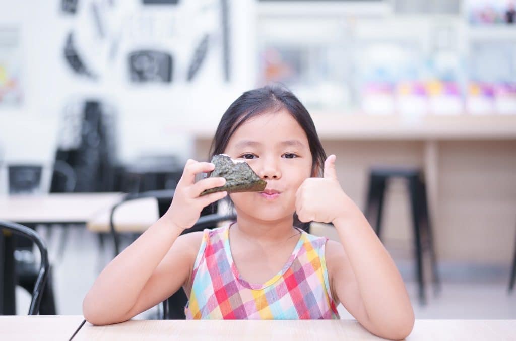 Child happily eating seaweed superfood with thumbs up