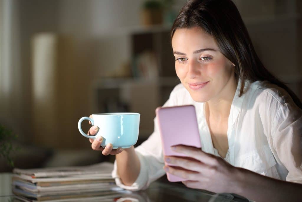 woman on phone with mug in living room at night.