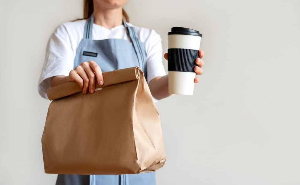 Cafe worker handing a paper bag and reusable cup, a practical example of sustainable packaging in daily service.