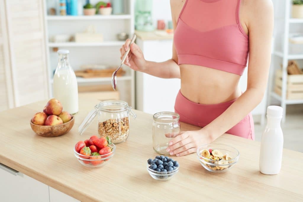 Woman meal prepping jars with granola and berries